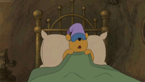 A sleepy cartoon bear laying in bed with a hat on.